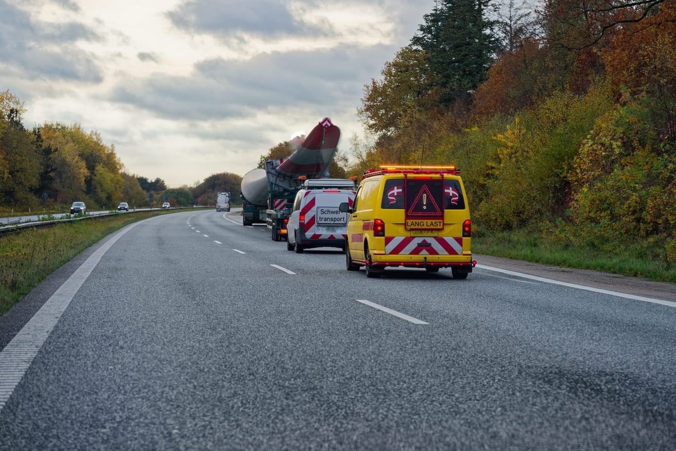 Ein gelbes Begleitfahrzeug mit der Aufschrift Lang Last sichert einen Schwertransport-Konvoi auf einer Landstraße ab.