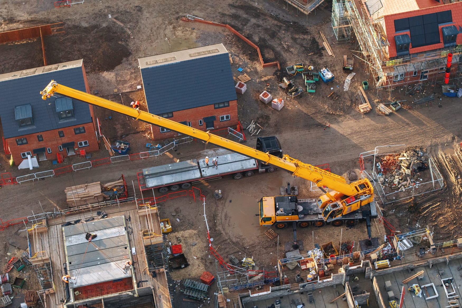Baustellenlogistik & Kranarbeiten in Deutschland | Direktspedition Luftaufnahme eines großen gelben Mobilkrans im Einsatz auf einer Baustelle für Wohnhäuser.