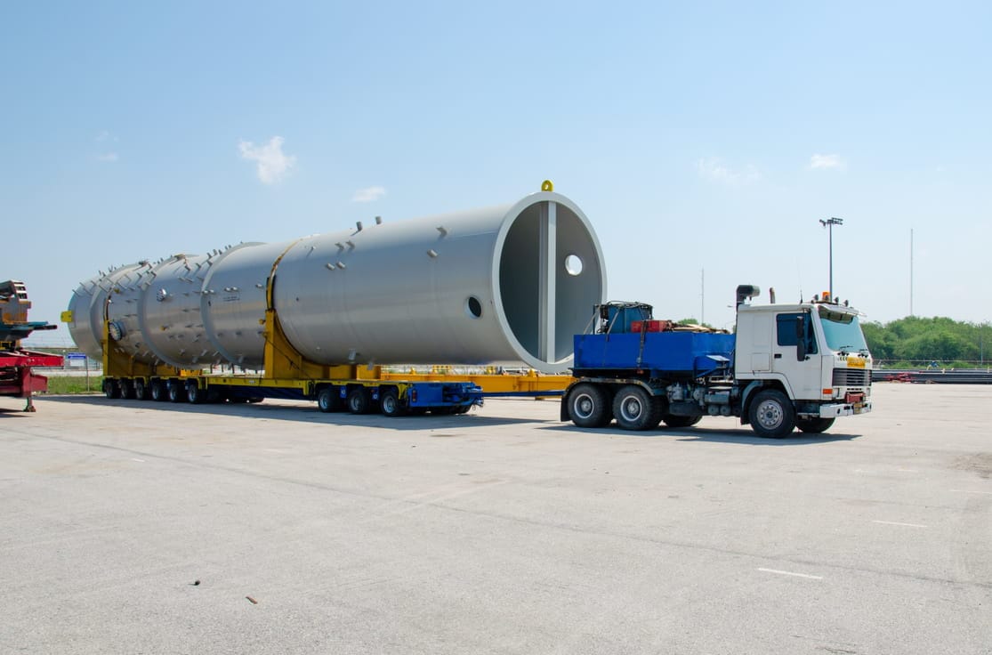 Ein vielachsiger Schwerlast-Modulauflieger transportiert ein riesiges zylindrisches Bauteil für eine Industrieanlage auf einem Werksgelände.